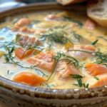 A bowl of creamy salmon soup garnished with dill and served with crusty bread.