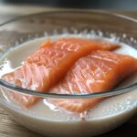 Fresh salmon fillet soaking in a bowl of milk.